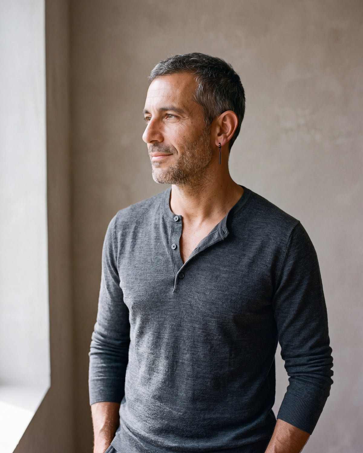 Second man in a fine-gauge charcoal-grey merino knit with a henley neckline wearing the black Atlas bar drop hoop earrings