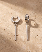 The whole silver-tone Atlas bar drop hoop earrings lying on warm travertine stone