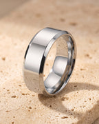 The whole silver-tone Atlas Beveled Edge Band Ring lying on warm travertine stone