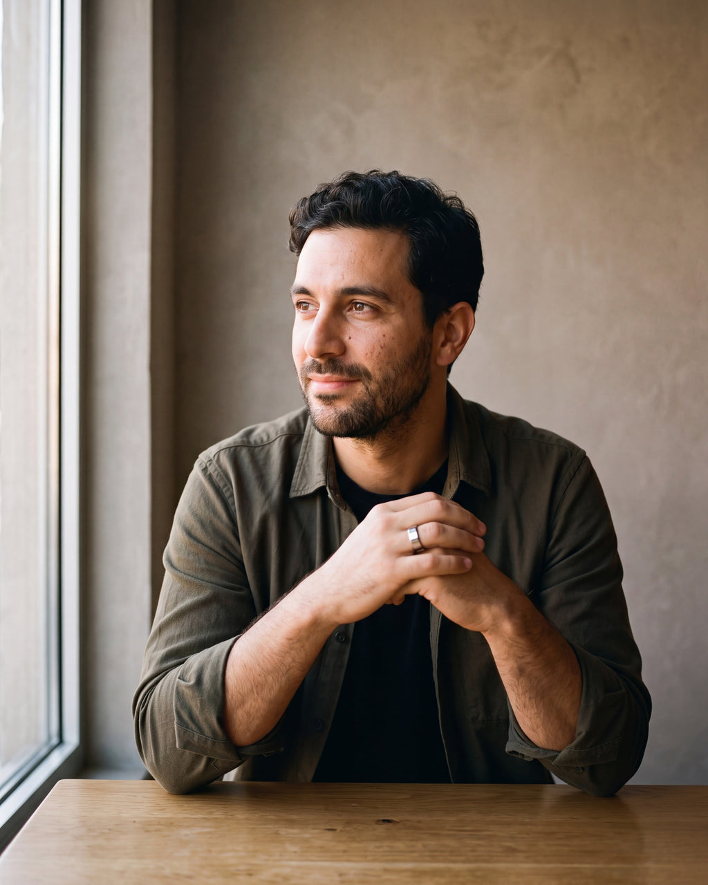 Man in a dark olive overshirt open over a black t-shirt by a window wearing the silver-tone Atlas Beveled Edge Band Ring