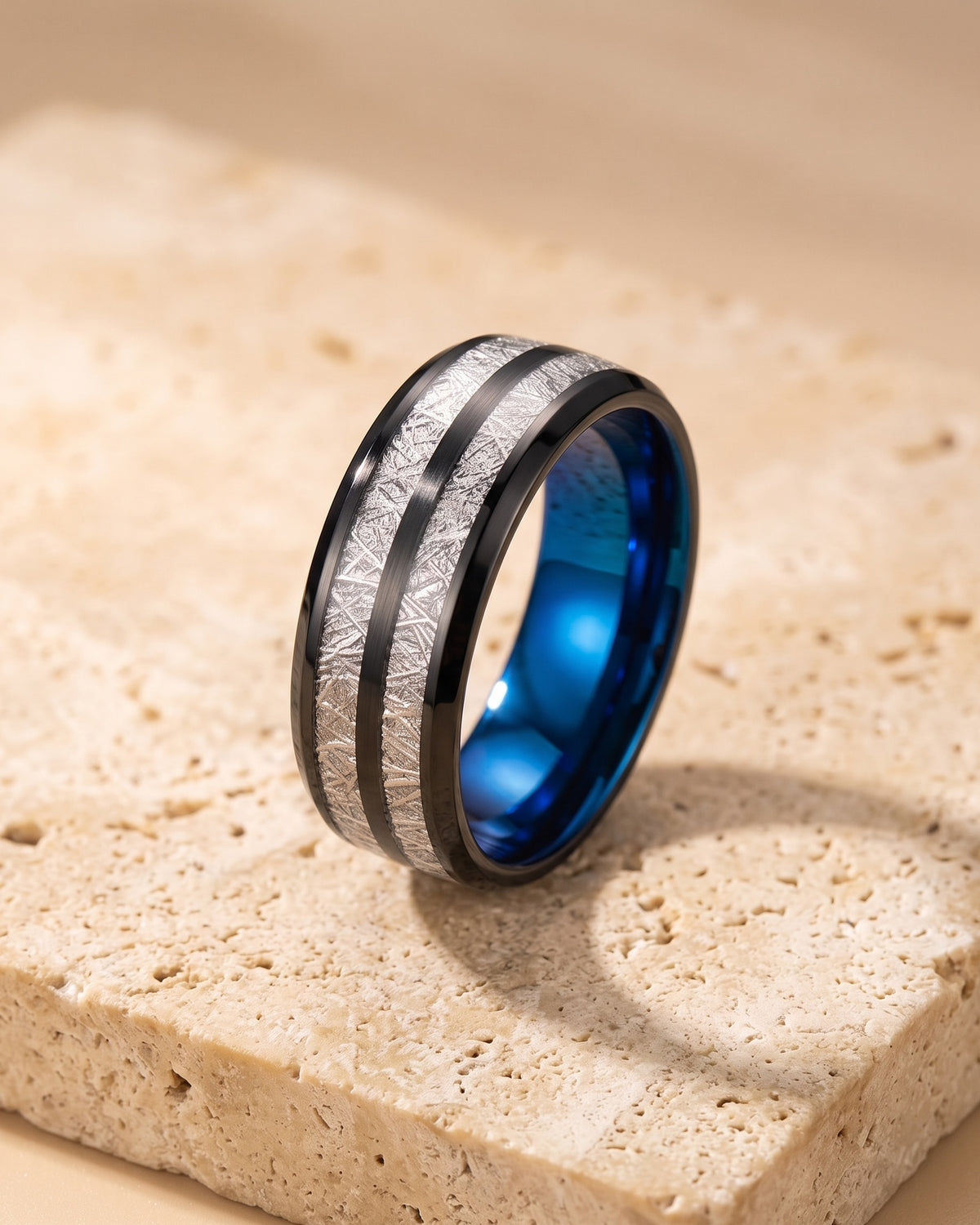 Atlas black and blue inlay tungsten ring standing on warm stone