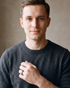 Man in a charcoal sweater with his hand on his chest, wearing the Atlas black and blue tungsten ring