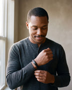 Man in a charcoal henley adjusting his sleeve wearing the black Atlas black braided leather magnetic bracelet