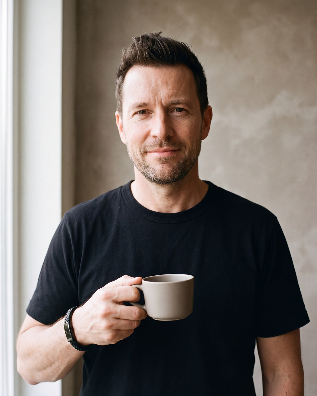 Man in a black T-shirt holding a coffee cup wearing the black Atlas black braided leather magnetic bracelet