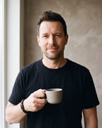 Man in a black T-shirt holding a coffee cup wearing the black Atlas black braided leather magnetic bracelet