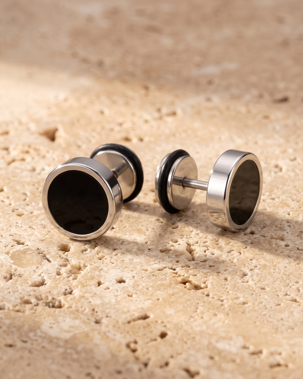 The whole silver Atlas Black Disc Stud Earrings lying on warm travertine stone