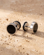 The whole silver Atlas Black Disc Stud Earrings lying on warm travertine stone