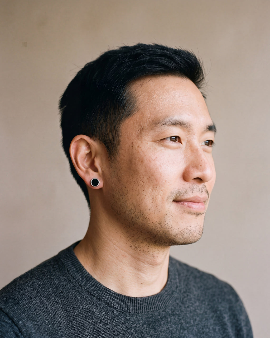 Man in a charcoal fine-gauge knit crew-neck sweater wearing the silver Atlas Black Disc Stud Earrings