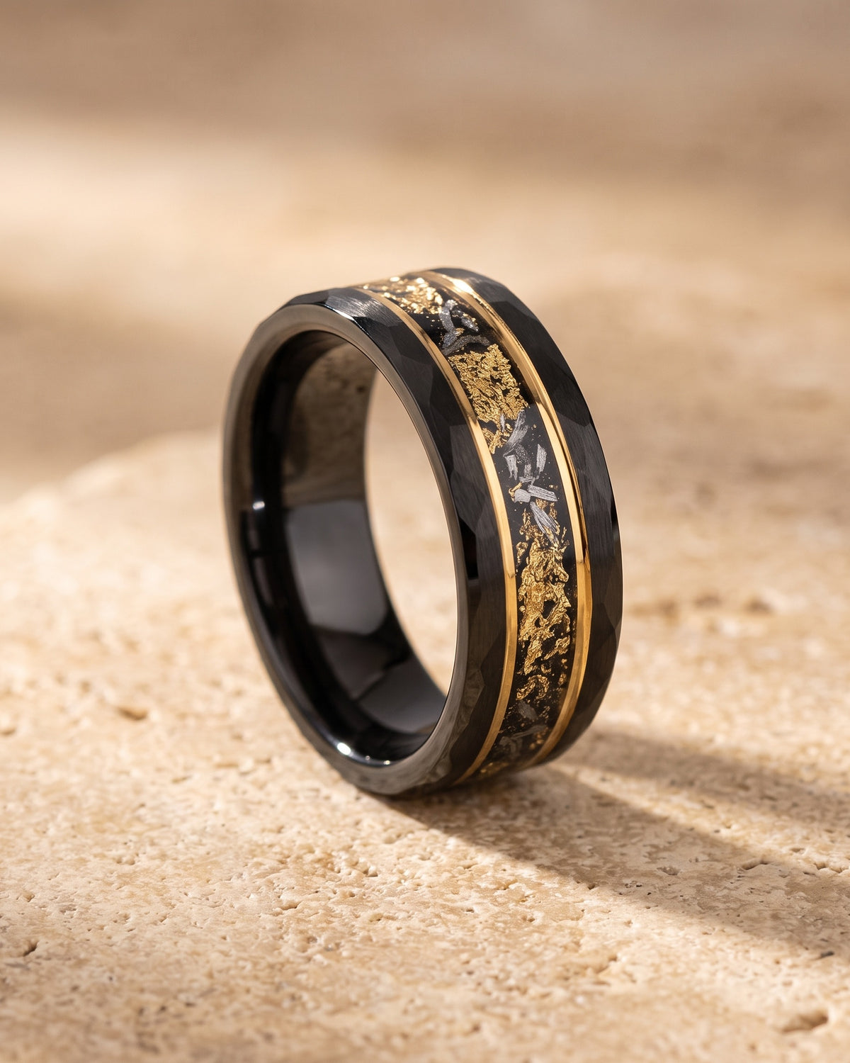 The whole black Atlas black gold-tone flake ring lying on warm travertine stone