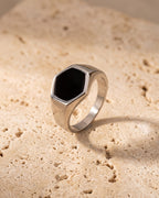 The Atlas black hexagon signet ring standing on warm stone