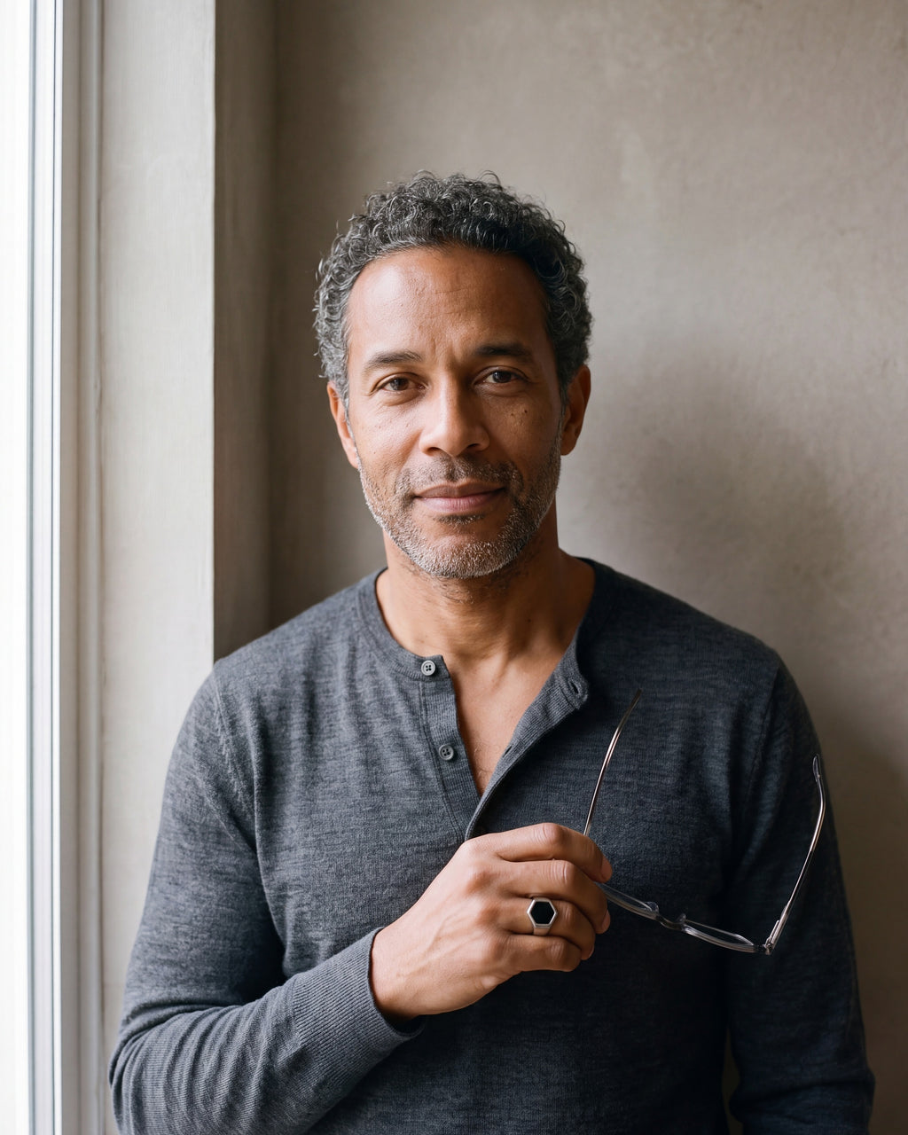 Man in a charcoal henley holding his glasses, wearing the Atlas black hexagon signet ring