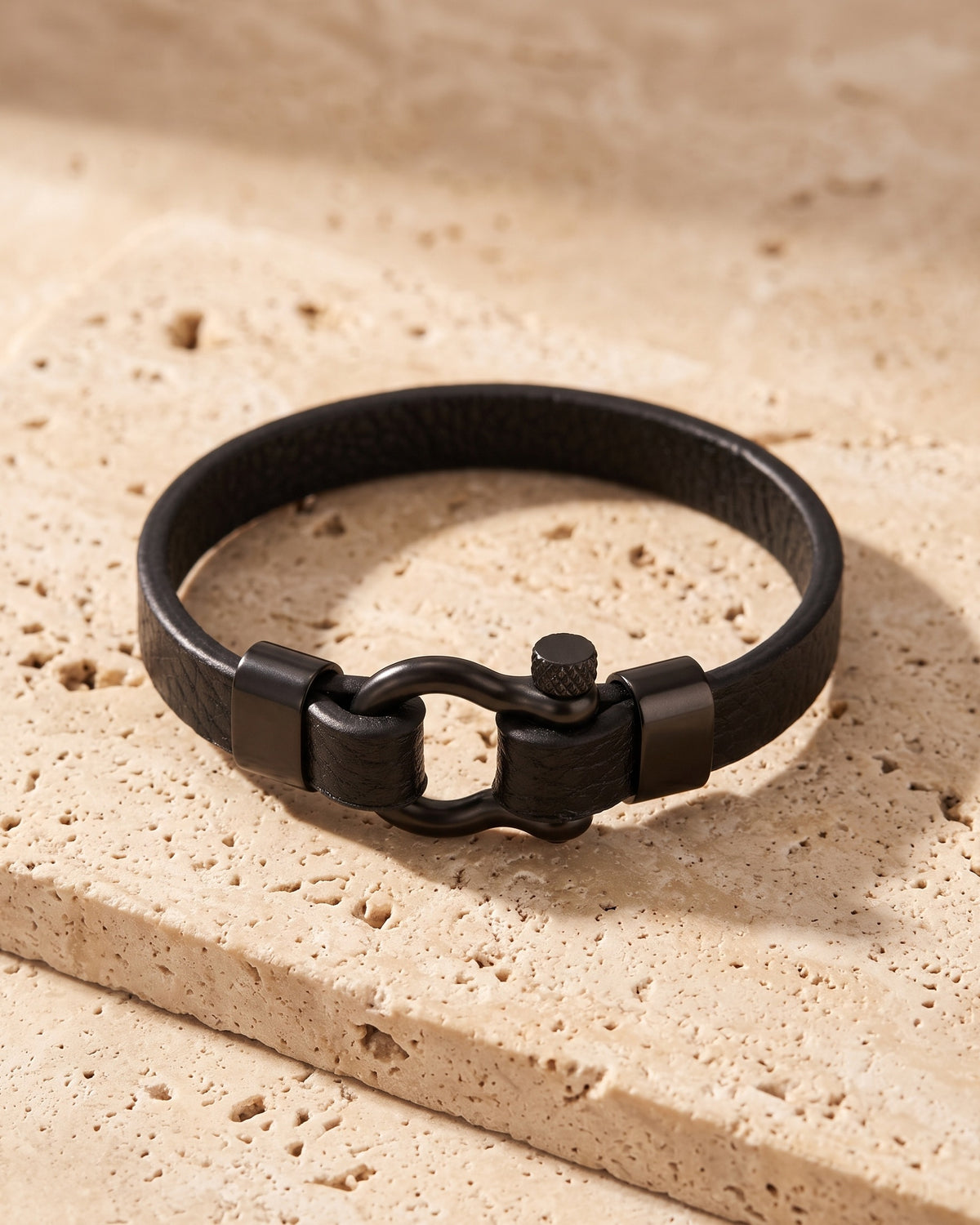 The Atlas black leather shackle bracelet closed, lying on warm stone