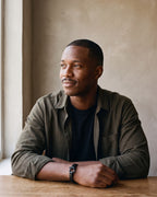Man in an olive overshirt seated at a wooden table, wearing the Atlas black leather shackle bracelet