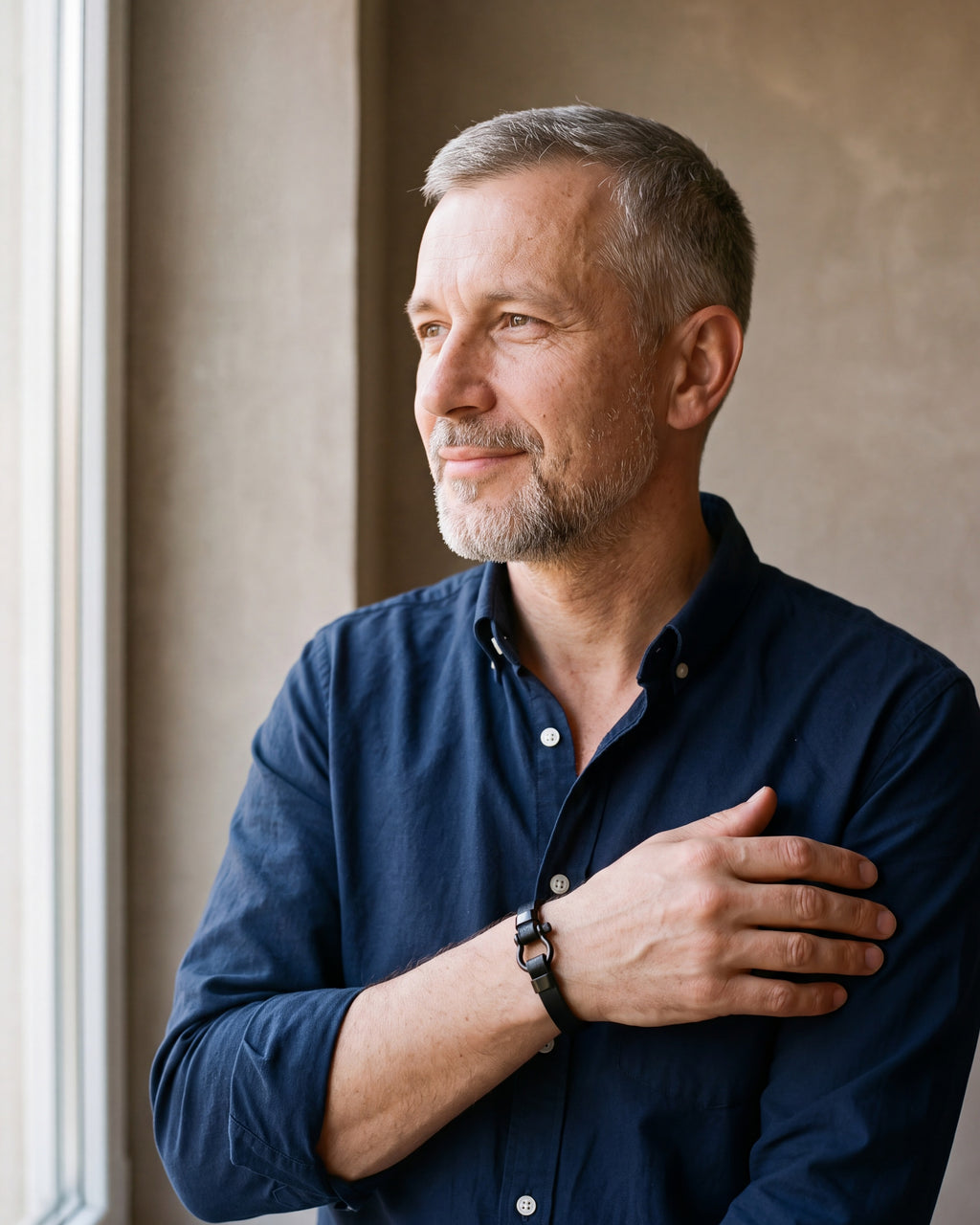 Man in a navy shirt by a window wearing the Atlas black leather shackle bracelet
