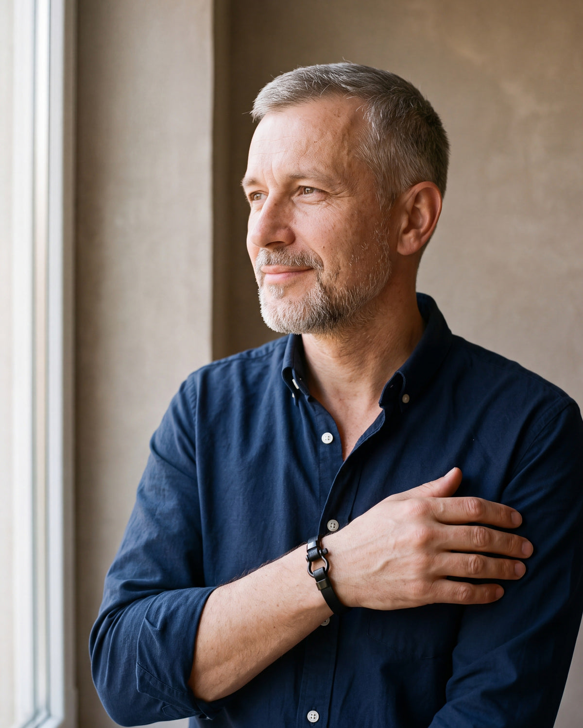Man in a navy shirt by a window wearing the Atlas black leather shackle bracelet