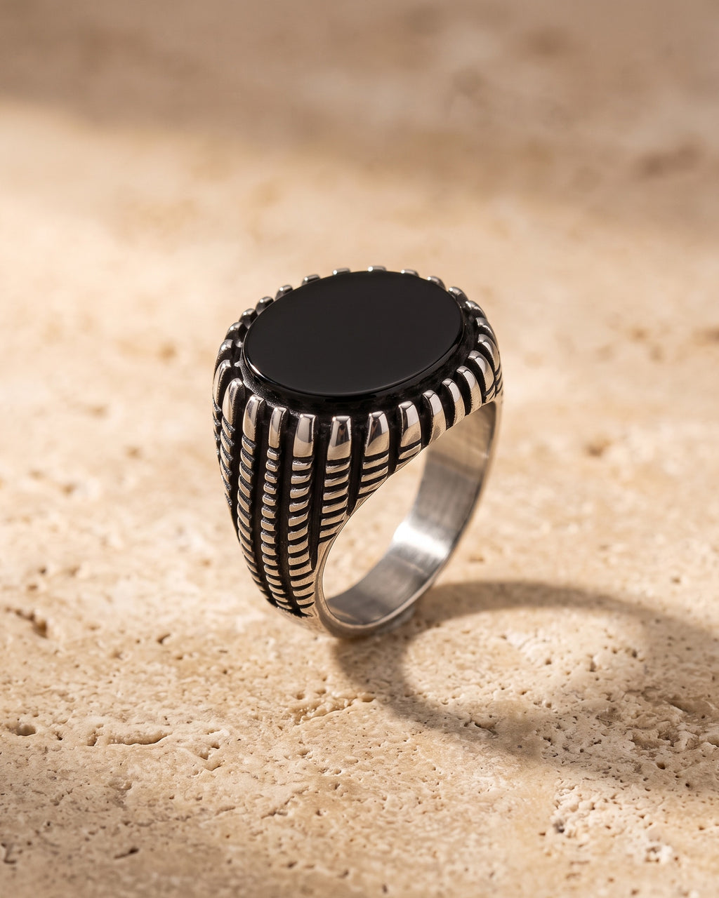 The Atlas black stone signet ring standing on warm stone, ribbed antique steel shoulders