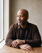 Man in a brown suede overshirt seated by a window, wearing the Atlas black stone signet ring