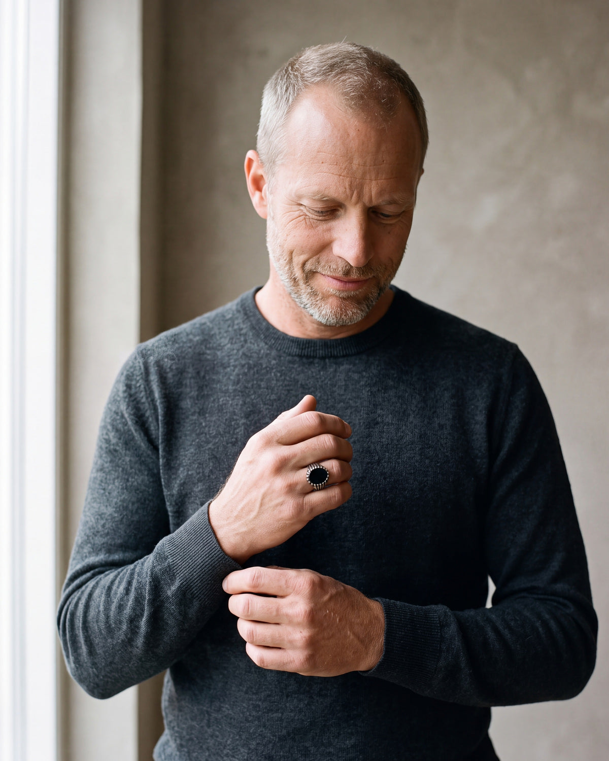Man in a charcoal sweater adjusting his cuff, wearing the Atlas black stone signet ring