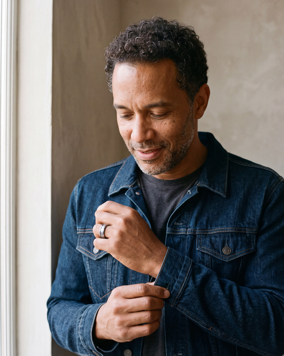 Man in a denim jacket adjusting his cuff, wearing the Atlas blue Celtic knot tungsten ring