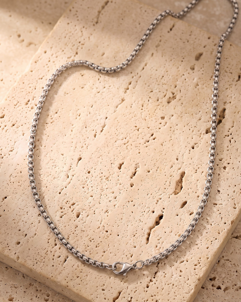 The silver Atlas Box Chain in Silver laid on warm travertine stone