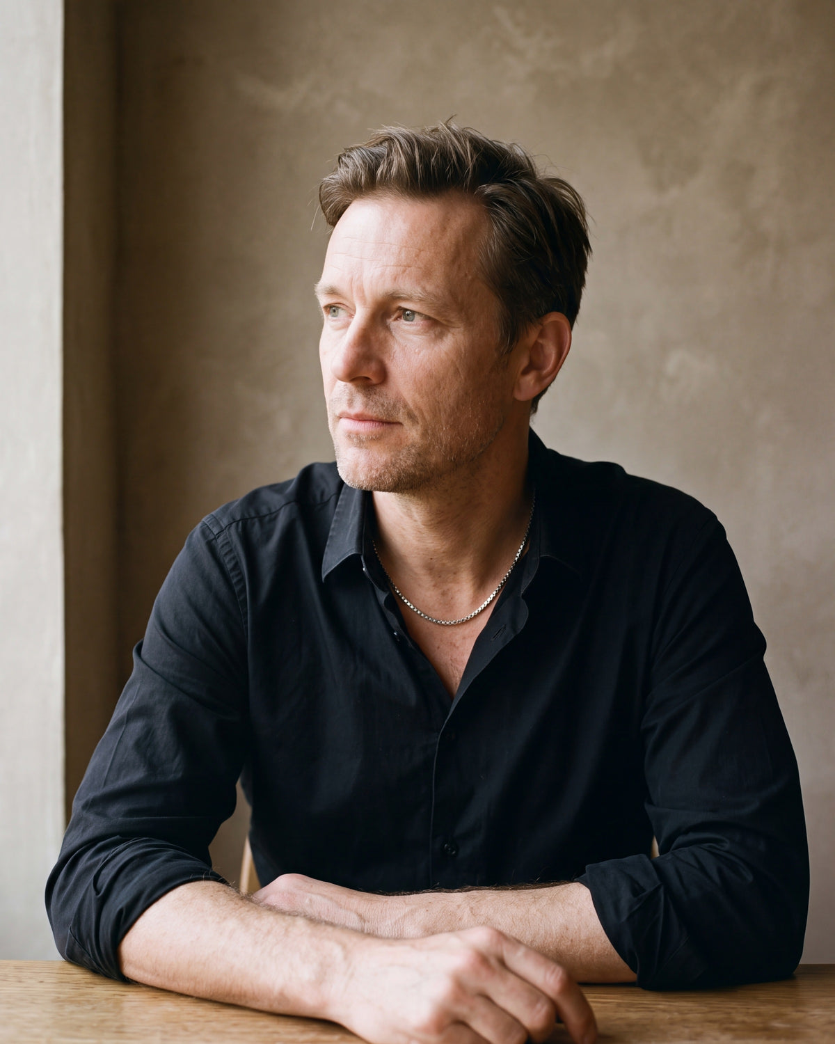 Man in a black fine cotton shirt by a window wearing the silver Atlas box chain with extender
