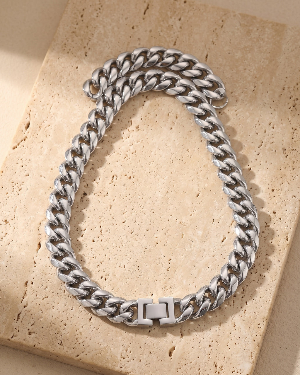 Silver Atlas Miami Cuban chain laid whole on warm stone, fold-over box clasp closed