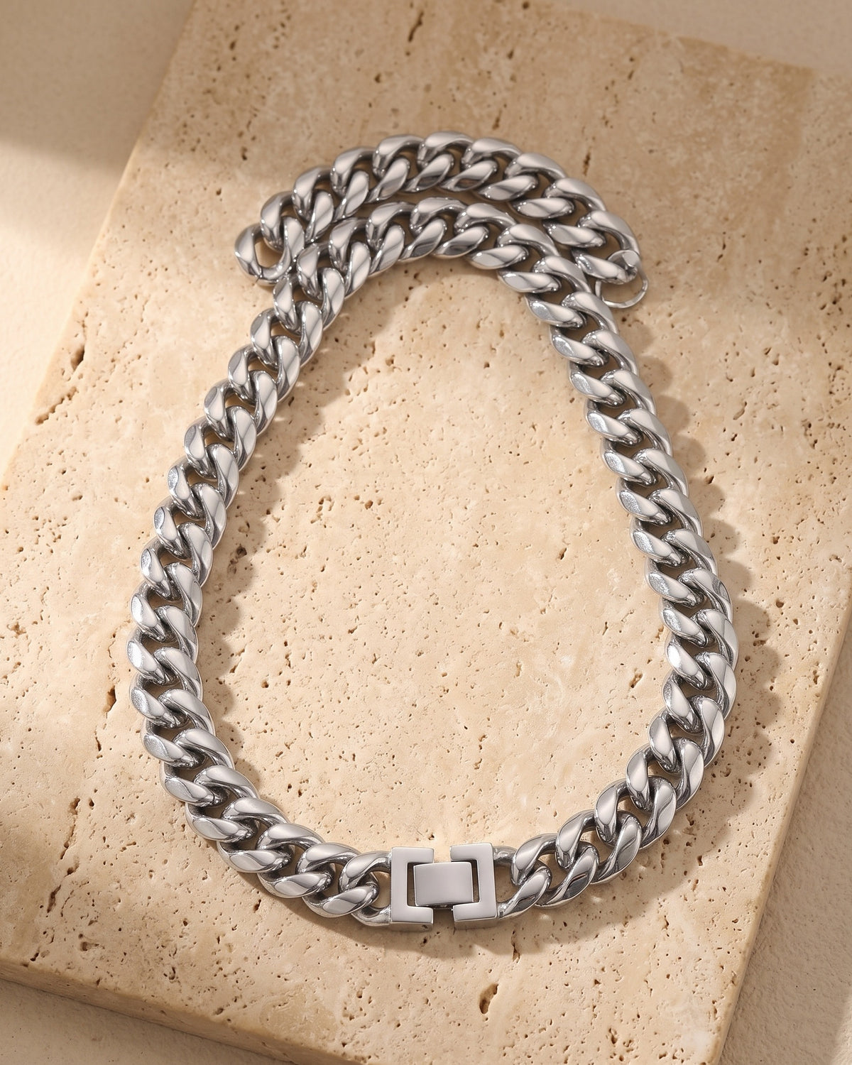 Silver Atlas Miami Cuban chain laid whole on warm stone, fold-over box clasp closed
