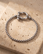 The whole silver-tone Atlas box link shackle bracelet lying on warm travertine stone
