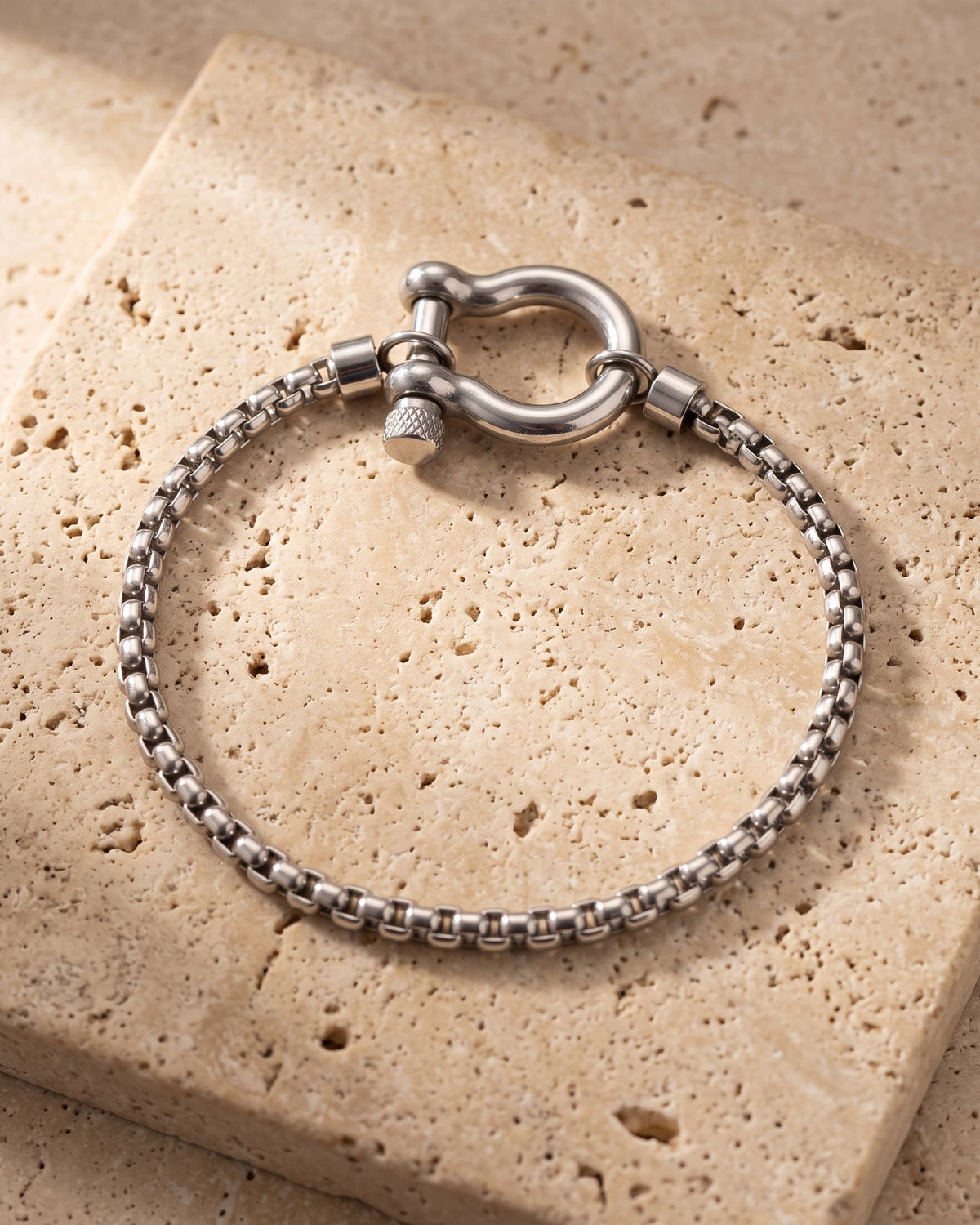 The whole silver-tone Atlas box link shackle bracelet lying on warm travertine stone