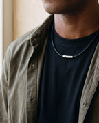 Close-up of the Atlas braided cord necklace and its steel clasp worn on a black T-shirt