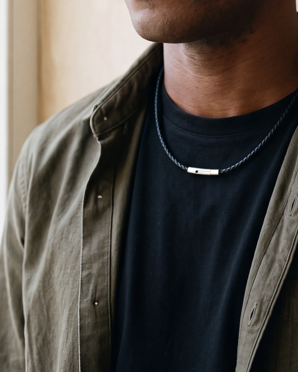 Close-up of the Atlas braided cord necklace and its steel clasp worn on a black T-shirt