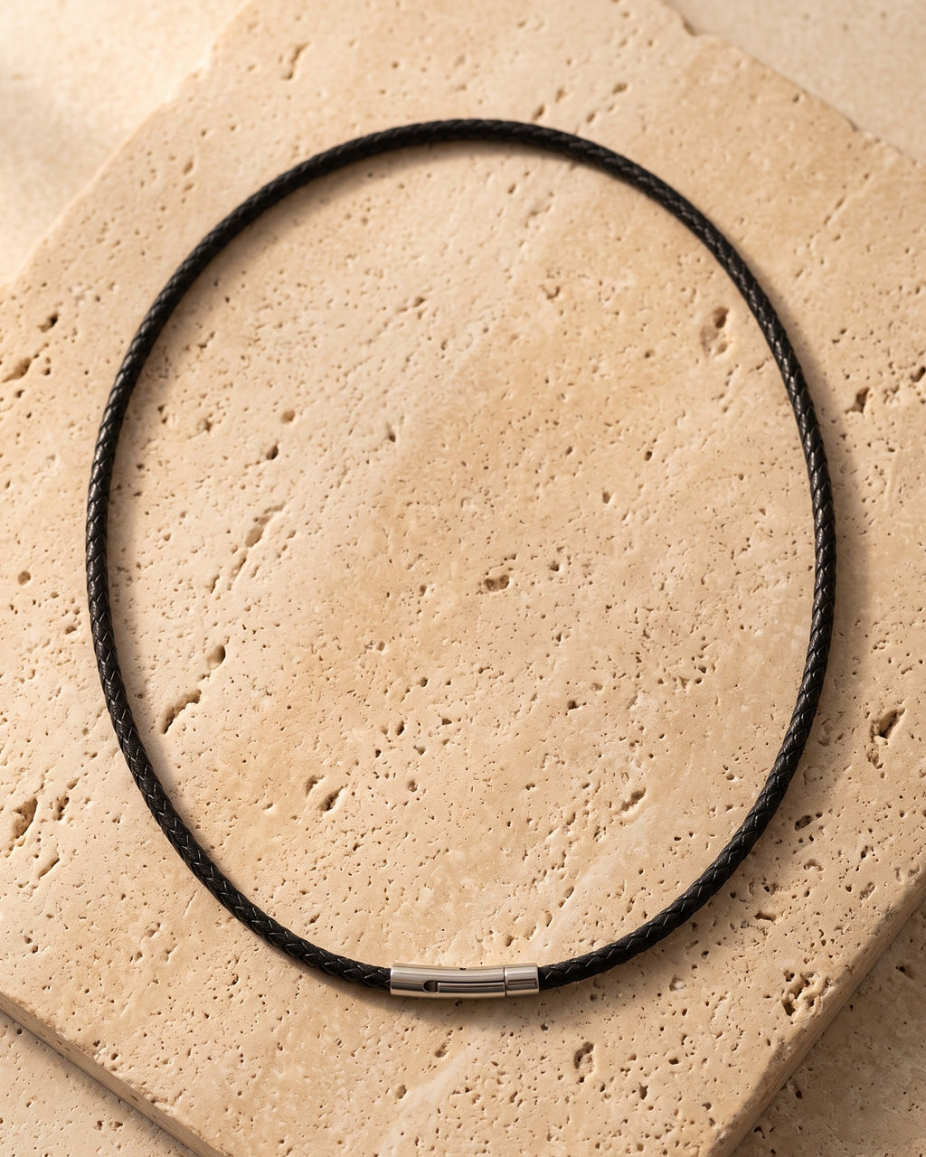 The whole Atlas black braided cord necklace on warm stone, steel clasp