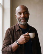 Man in a brown suede overshirt holding a coffee cup, wearing the Atlas braided leather magnetic bracelet