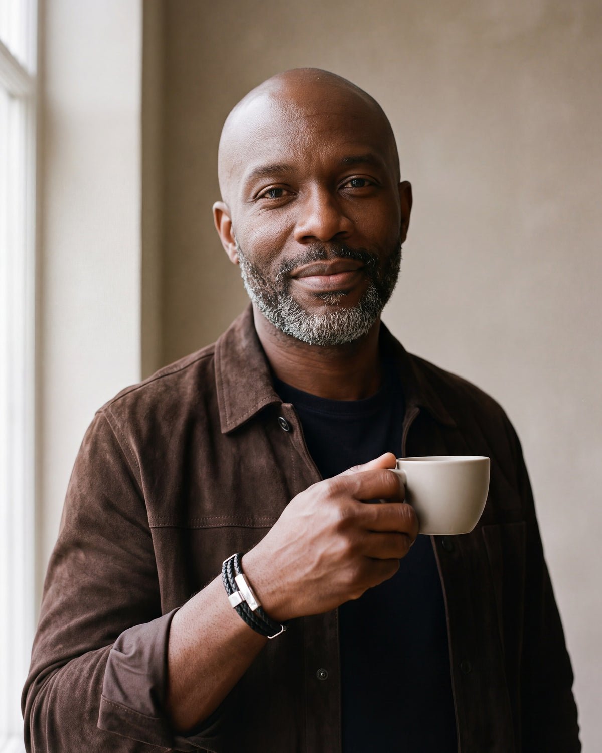 Man in a brown suede overshirt holding a coffee cup, wearing the Atlas braided leather magnetic bracelet