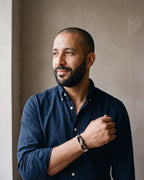 Man in a navy oxford shirt by a window wearing the black and silver-tone Atlas braided leather shackle bracelet
