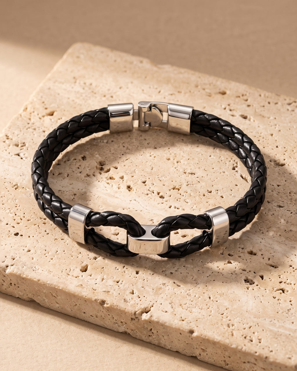 The whole black and silver-tone Atlas braided leather shackle bracelet laid on warm stone