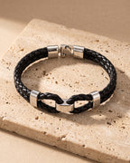 The whole black and silver-tone Atlas braided leather shackle bracelet laid on warm stone