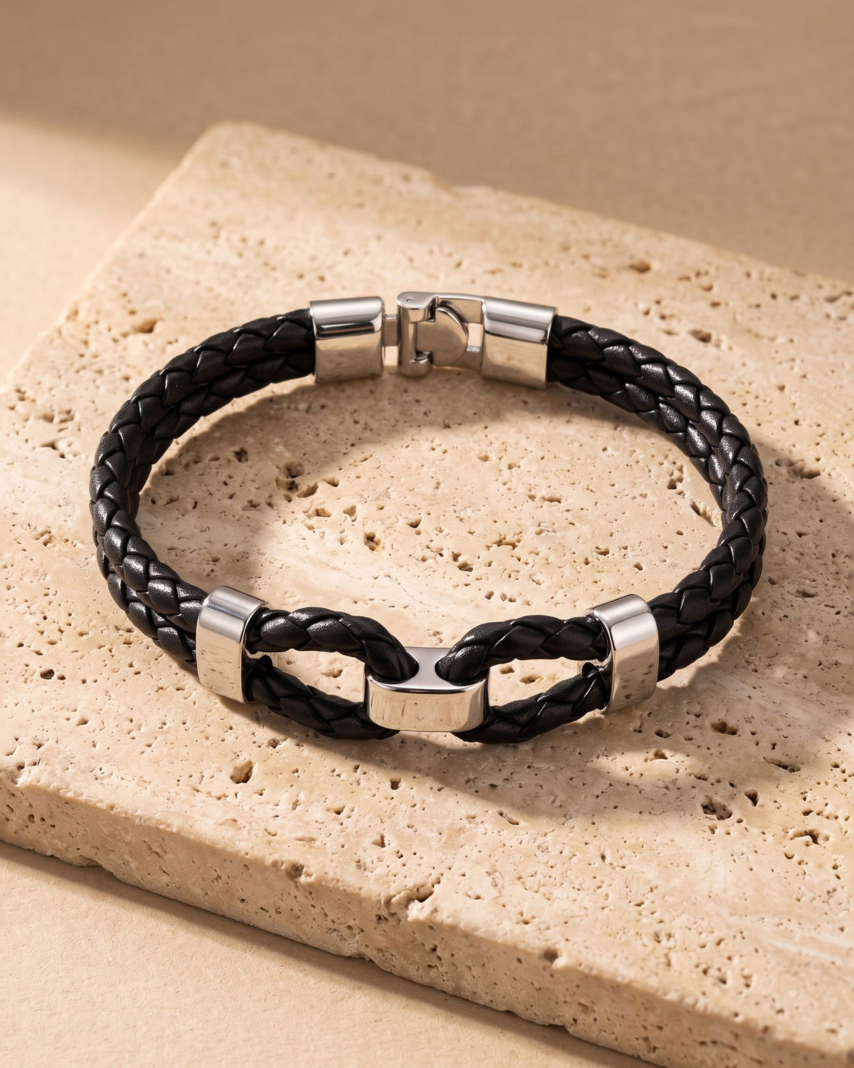 The whole black and silver-tone Atlas braided leather shackle bracelet laid on warm stone