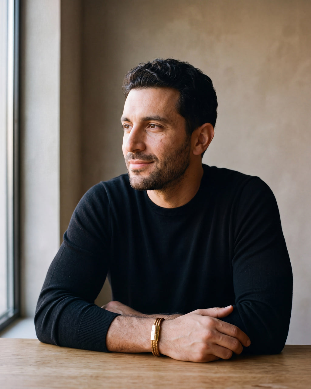 Man in a black merino crew-neck sweater wearing the gold-tone Atlas Braided Magnetic Bracelet