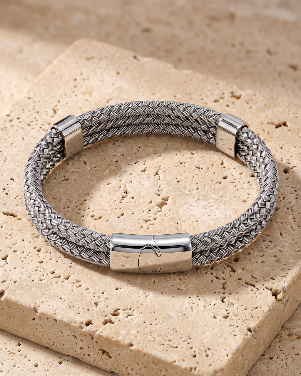 The whole silver-tone Atlas Braided Magnetic Bracelet lying on warm travertine stone