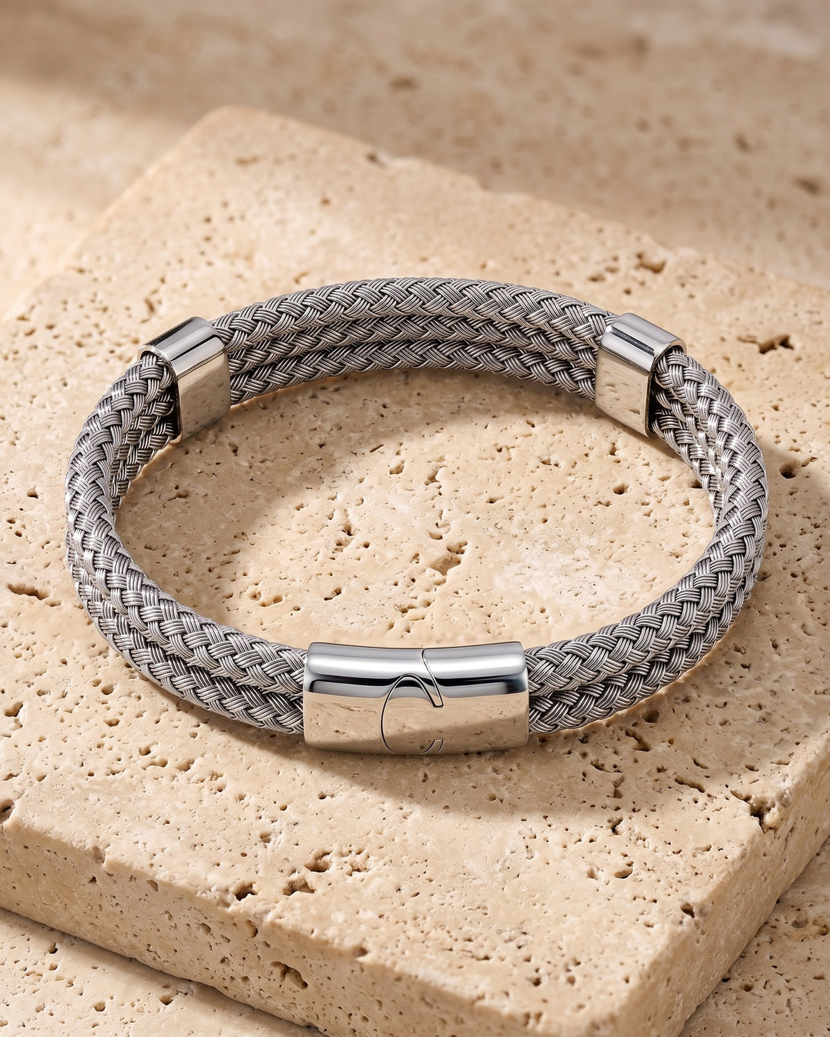 The whole silver-tone Atlas Braided Magnetic Bracelet lying on warm travertine stone
