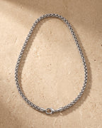 Entire Atlas braided wheat chain in silver-tone steel, lying flat on warm stone