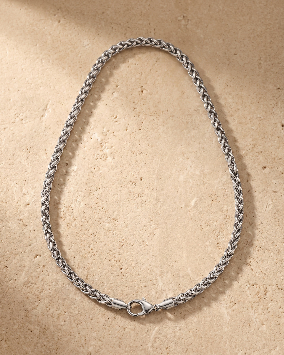 Entire Atlas braided wheat chain in silver-tone steel, lying flat on warm stone