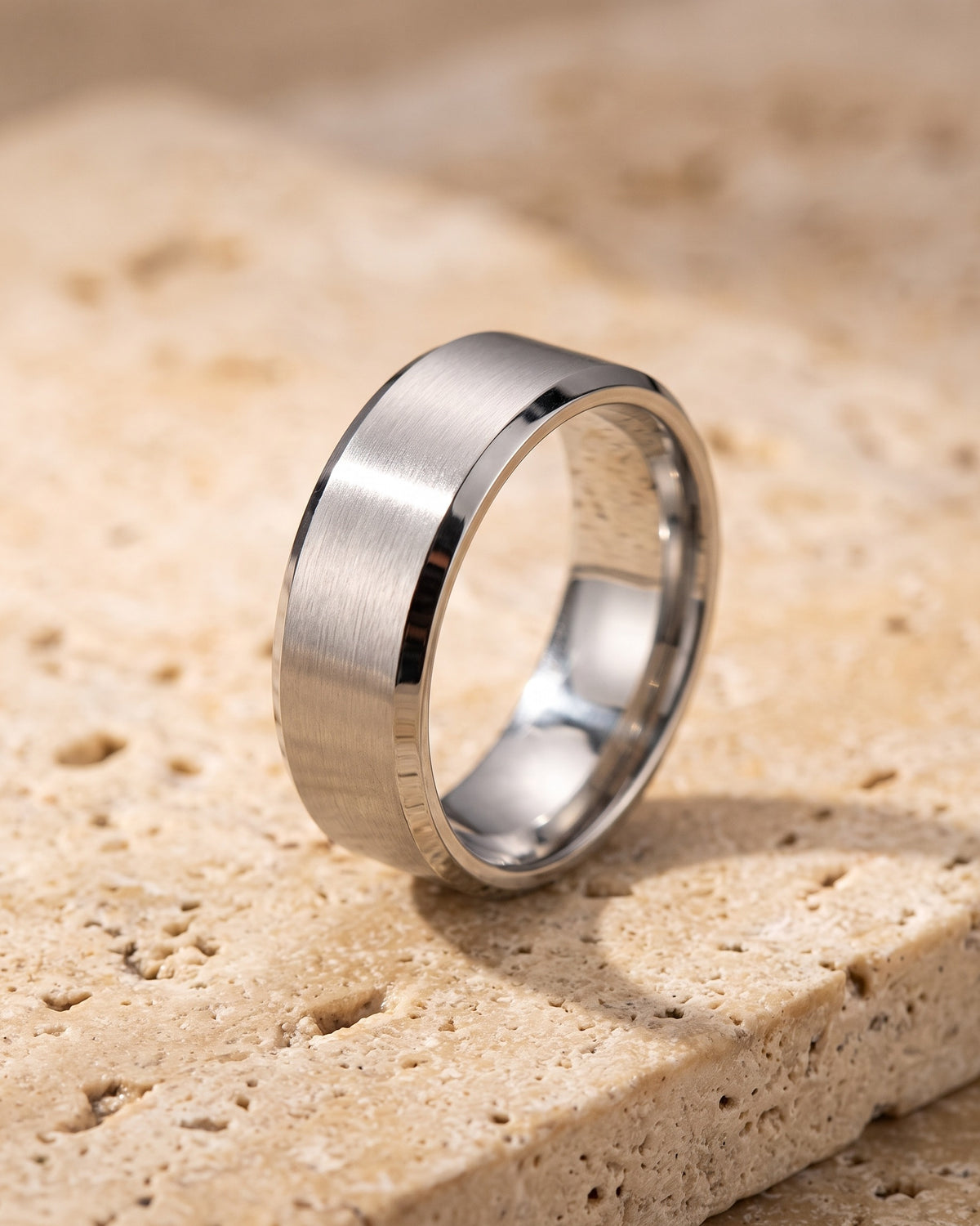 Silver Atlas brushed beveled band ring standing on warm stone