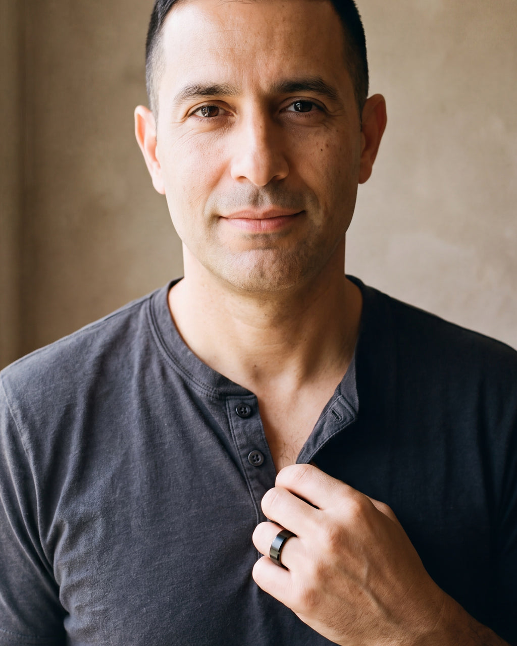 Man in a charcoal henley with his hand on his chest, wearing the black Atlas brushed beveled band ring