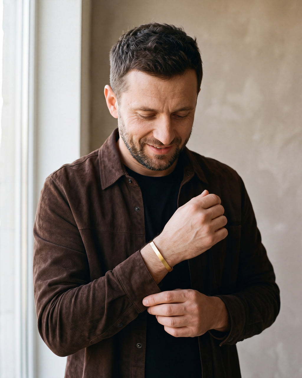 Man in a brown suede overshirt adjusting his sleeve wearing the gold-tone Atlas brushed cuff bracelet