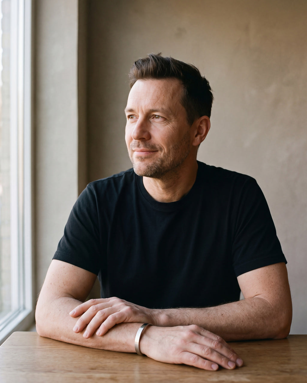 Man in a black T-shirt seated at a wooden table wearing the silver-tone Atlas brushed cuff bracelet