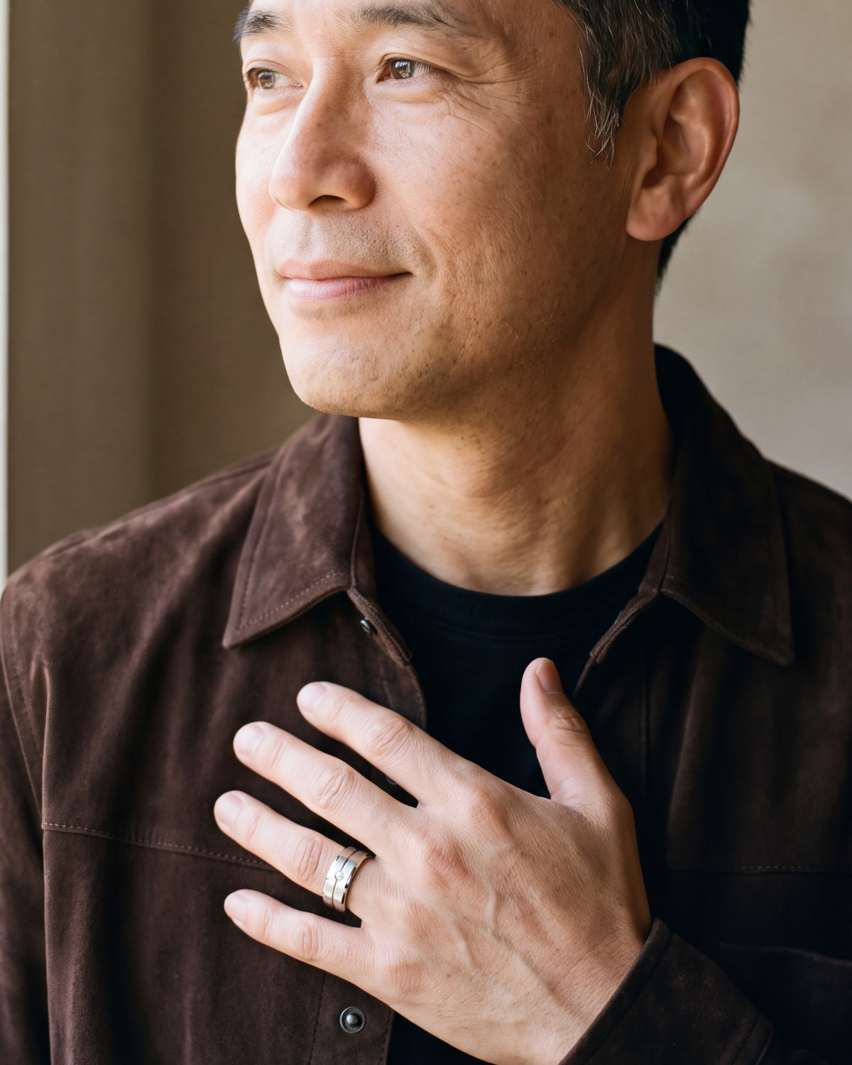 Man in a brown suede overshirt with his hand on his chest, wearing the silver Atlas brushed cubic zirconia band ring