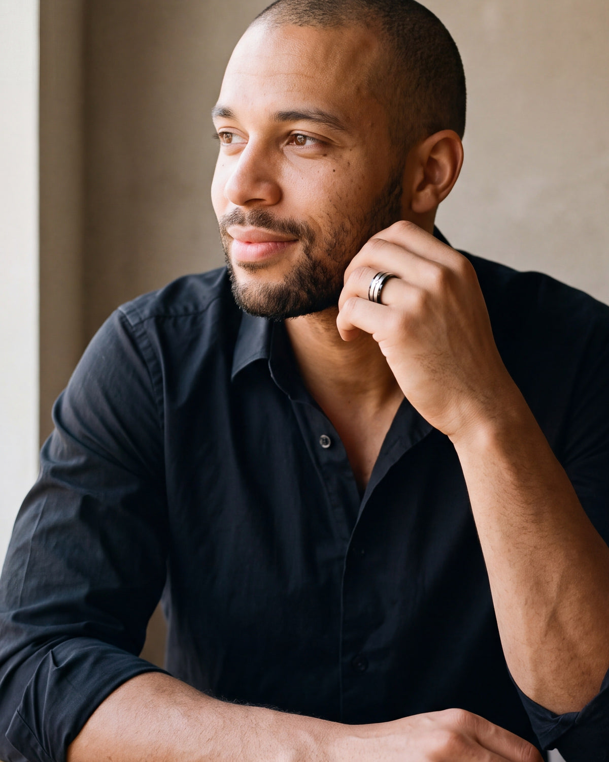 Man in a black shirt seated at a table, hand at his face, wearing the black and silver Atlas cubic zirconia band ring