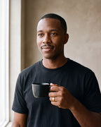 Man in a black T-shirt holding a coffee cup, wearing the gold-tone Atlas double groove ring
